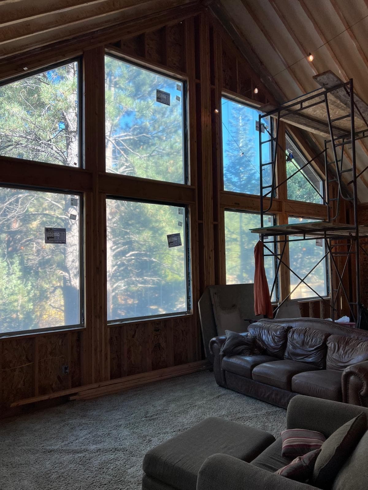 Great room mid-build — window wall framed and glazed, the ceiling still open, scaffold set before the board goes on.