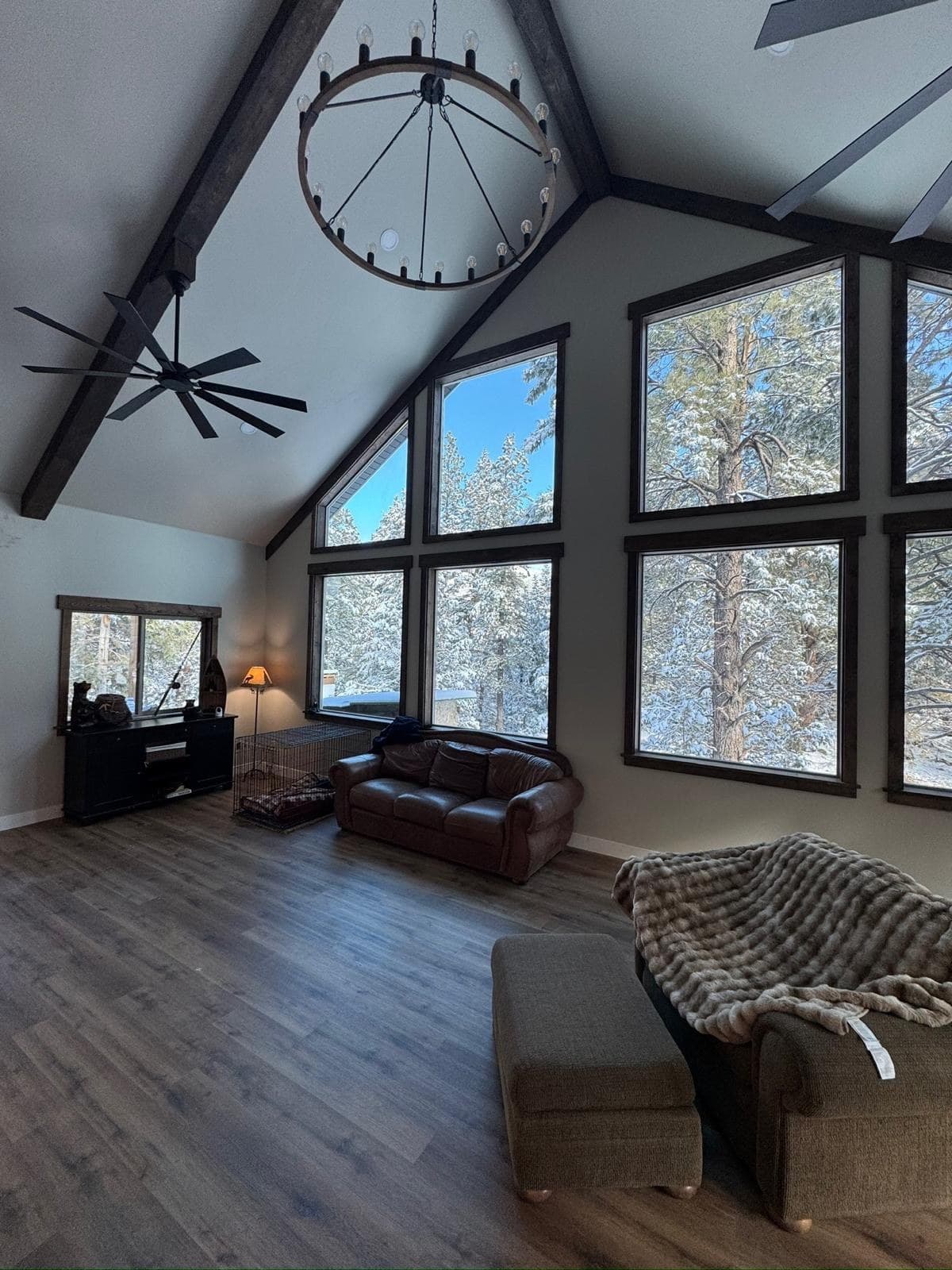 Vaulted great room, finished — smooth ceiling planes meeting stained beams, the window wall trimmed out square, new flooring run to the glass.